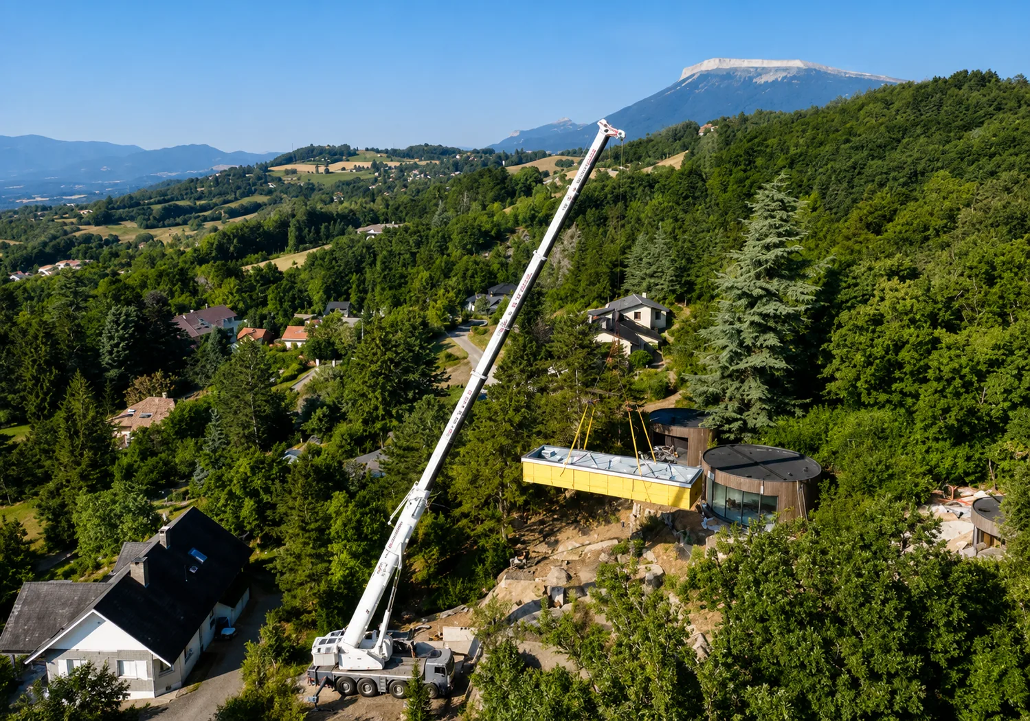 Crane lowering a prefabricated pool into a wooded hillside site